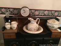 Full view of the pitcher and basin with additional small ceramic items and mantel clock in background.