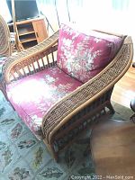 Front-right perspective of rattan armchair showing floral seat and back cushions and woven rattan armrest design.