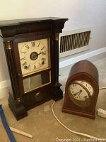 Full view of both clocks showing the dark wood mantle clock and the smaller beehive style clock side by side on floor.