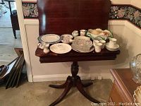 Vintage wooden folding game table with a curved backboard and various ceramic and glass items arranged on top.