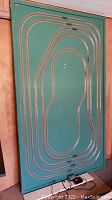 Green rectangular board with multiple loops of N gauge train tracks mounted on it, showing the overall layout and condition.