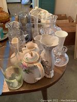 Photo showing variety of glass and ceramic vases, pitchers, candy dishes and baskets, highlighting floral ceramic pieces and clear cut glass items.