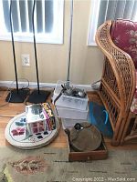 Wide shot of various items on wooden floor including vintage metal skates, plastic containers, wooden tray with utensils, dustpan, floral mat, and wicker chair.