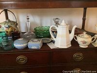 Multiple items displayed on wooden surface: jasperware pieces, pitchers, teapots, glass bowls, decorative jar