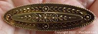 Top view of oval bar brooch held in palm showing floral wirework and beaded border