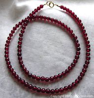 Full view of garnet bead necklace showing round deep red beads and gold filled clasp against white fabric background.