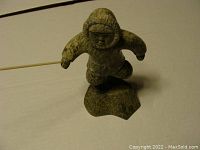 Front side of the Inuit sculpture showing the figure holding a spear with one hand and the other hand empty, wearing detailed parka clothing and standing on a stone base.