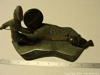 Side view of Inuit soapstone sculpture showing figure with drum and seal on a leather string
