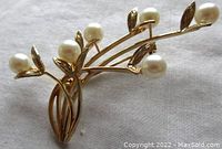 Front angled view of the brooch on fabric background showing six branches with engraved leaves and six round pearls.