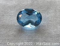 Oval-shaped faceted blue topaz gemstone on fabric background showing its cut and transparency.
