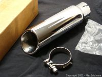 Exhaust tip with clamp and cardboard box showing the full assembly and packaging.
