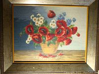 Whole framed petit point needlepoint floral artwork showing vibrant red poppies, white daisies, and blue flowers in beige vase with blue background.