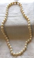 Full view of the vintage Akoya cultured pearl necklace showing the strand of pearls and gold clasp against a white fabric background.