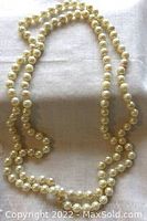 Full view of creamy white, approximately 35-inch long pearl necklace laid out on white fabric, showing the length and round shape of pearls