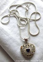 Full view of the sterling silver heart pendant on the chain showing openwork and blue sapphire center.