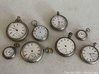 Group of seven antique pocket watches with visible white dials marked mostly Arabic numerals and some Roman numerals; all silver cases varying sizes.