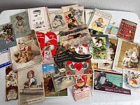Wide view of assorted antique postcards and advertisements laid on table, showing colorful and detail-rich early 1900s prints depicting children and holiday themes.