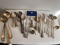 Overview of 30 pieces of various silverplate and coin silver flatware and serving pieces on a table.
