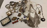 Box with varied vintage costume jewelry items including watches, necklaces, brooches, and earrings spread out on surface.
