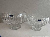 Two clear Marquis Waterford crystal bowls of different sizes, both with pedestal bases and geometric cut designs, displayed on a white surface against a beige wall.