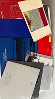 Photo showing multiple Porsche brochures and fold-out posters stacked, including red cover brochures and one blue Porsche 928 brochure