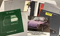 Overview photo of all fifteen Porsche factory car brochures and fold-out posters arranged on a surface showing various front covers and sizes.
