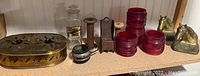 Full view of all items displayed on a shelf including the brass horse bookends, red lantern globes, wooden rocking chair bank, fly rod reel, and medical jar.