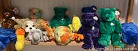 Photo showing 10 plush TY Beanie Babies and Buddies including various colored bears and animal figures such as an elephant and a chick, arranged on shelf.