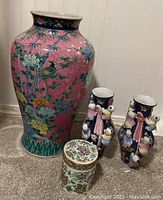 Pink decorated tall floor vase, white ginger jar, and black pair vases placed together on carpeted floor.