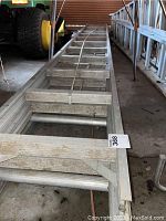 Photo showing full length of the aluminum ladder resting on ground with visible flat rungs and side rails.