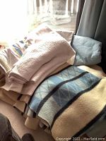 Blue and cream patterned wool blanket with other blankets folded underneath, shown on a bed near a curtain.