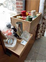 Wooden liquor box filled with various colored candles, a metal mould, glass ashtrays, and orange wax crayons in plastic.