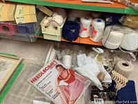 Shelf with assorted crochet cotton spools, skeins, and a vintage Needlecraft pattern book visible