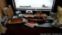 Wide view showing assortment of wooden serving boards, glass candleholders, stainless steel covered dish, and napkin rings near window.