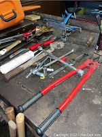 Tools arranged on a surface including bolt cutters, pry bars, pliers, and an assortment of hand tools.