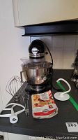 Front view of stand mixer on countertop with bowl, attachments, and manual arranged around base