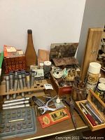 Overview of the lot showing various leather crafting tools including stamps, dyes, cutting tools, and accessories arranged on a wooden surface.