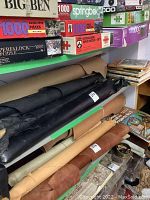 Shelf with multiple leather rolls in black and lighter colors beneath puzzle boxes and stack of books