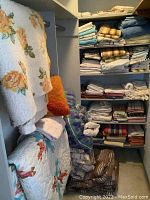 Shelves and wall with folded quilts, pillows, comforters and linens in various patterns and colors including floral and stripes.
