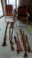 Two folding chairs made of aluminum with orange and black macrame seats and backs, placed beside several macrame hangers in various colors and patterns on the floor.