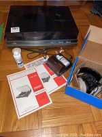 Overall view of turntable assembly with dust cover closed, headphones in box, cleaning fluid and manuals spread out