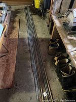 Photo showing all ten pieces of rebar laid on a concrete floor inside a garage near boots and wooden items.