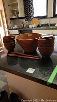 Photo showing the full set of one large mixing bowl, eight smaller bowls, and wooden fork and spoon on a countertop.