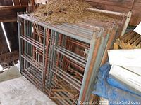 Stacked metal scaffolding side frames showing multiple frames with cross-bracing and surface rust