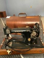 Black Singer sewing machine with copper-colored metal lid on table, shows side profile, power cord attached, gold branding visible