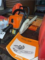 Full view of chainsaw, carrying case, oil bottles and manual on workbench