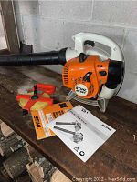 Stihl leaf blower, measuring tape, and two manuals on wooden bench