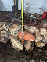 Weed trimmer head with orange guard and yellow shaft resting on firewood.
