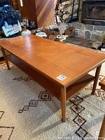 Front angled view of teak coffee table showing tapered legs, lower shelf, and top surface.