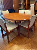 Oval teak table assembled with six leather-upholstered teak chairs around it.